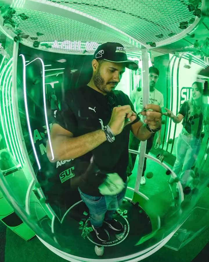 Interior da cabine de vento em operação, com vouchers, bolinhas e papel picado em suspensão no fluxo de ar.